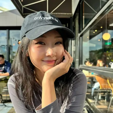 Victoria Sun smiling in a black cap at an outdoor cafe